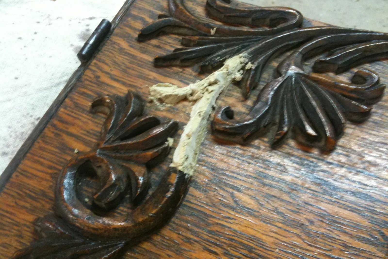 Close-up of intricately carved wooden panel with damaged wood and remnants of gray putty filling a broken section.