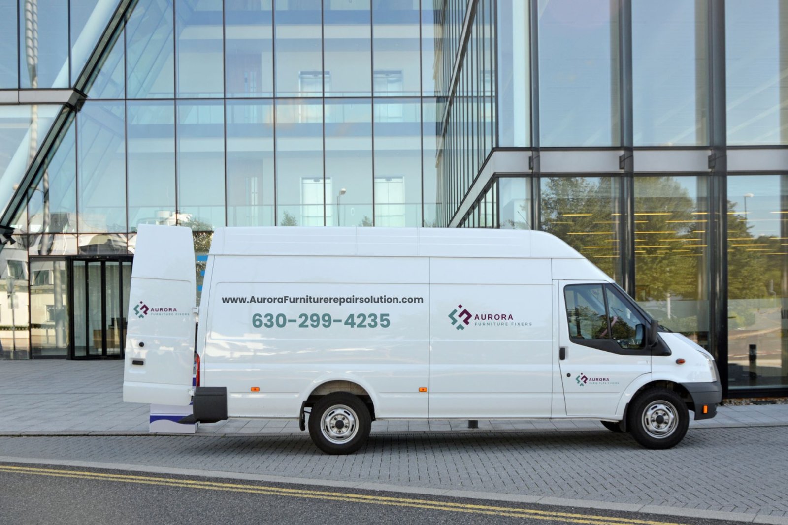White service van parked outside a modern glass building, displaying the company name and contact information on its side.