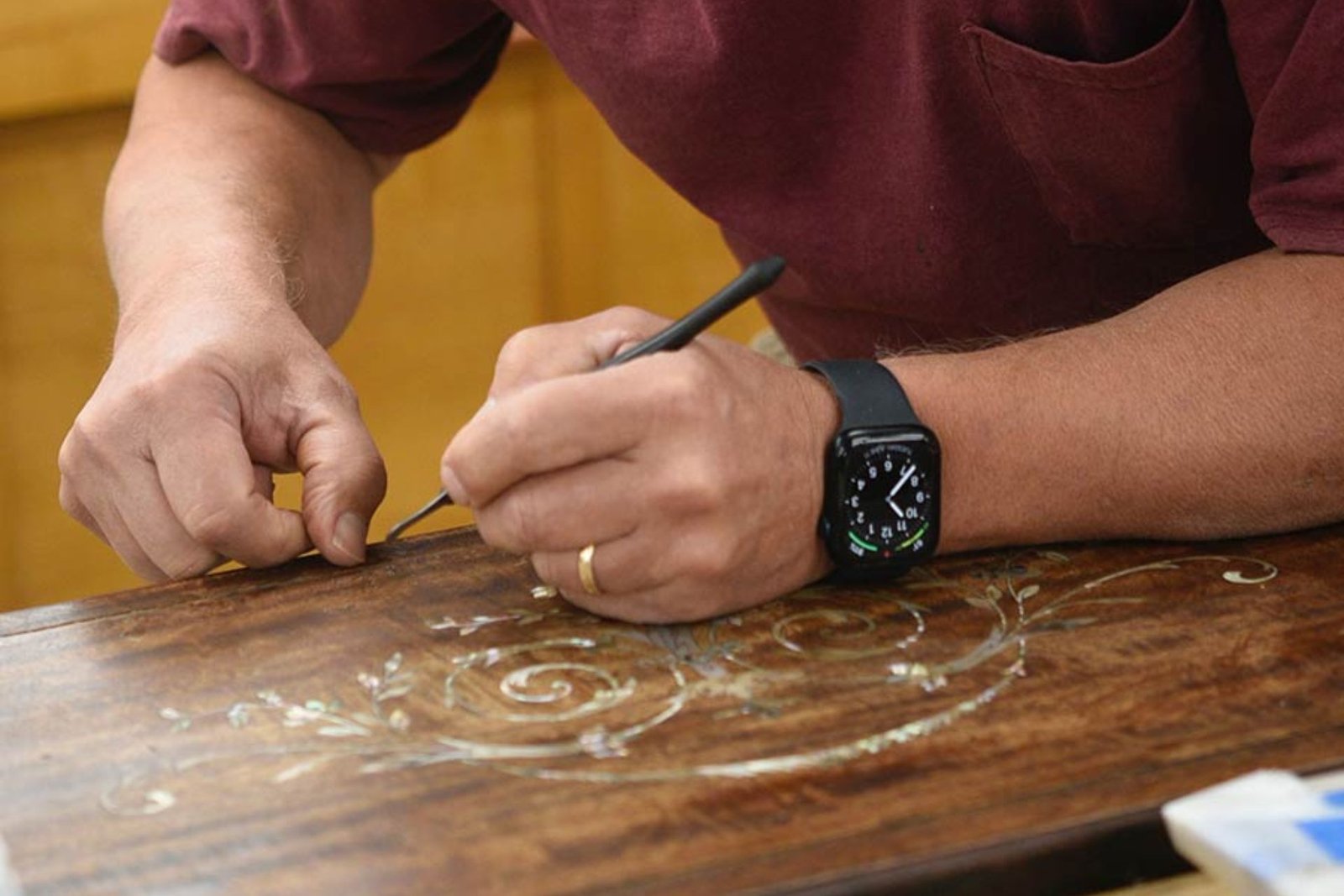 A man at a wooden table, concentrating on his task, with a watch visible on his wrist.