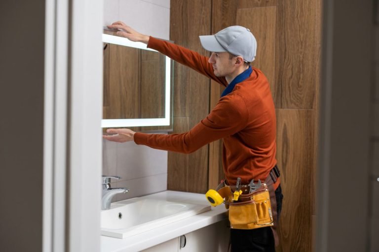 A man wearing a hat adjusts a mirror as part of a furniture service task.
