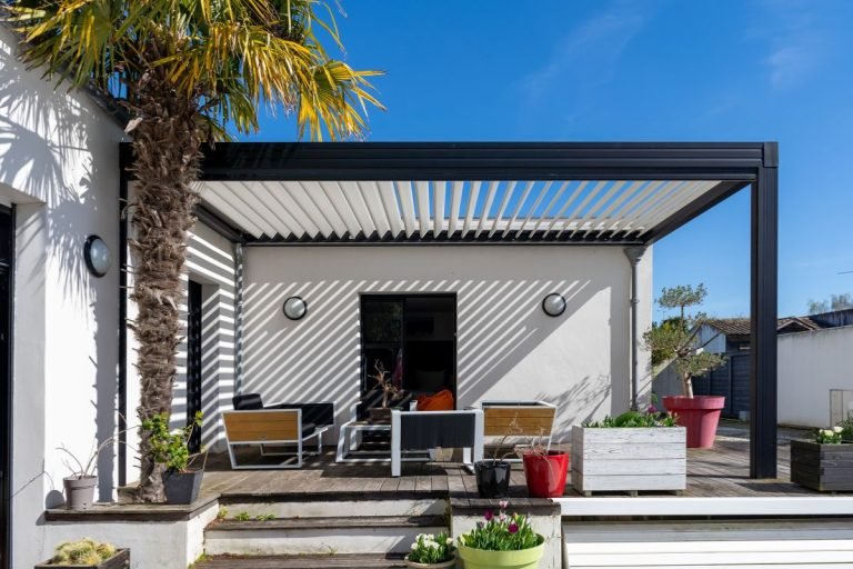 A patio featuring a white roof, palm trees, and furniture service, creating a tropical and inviting outdoor space.