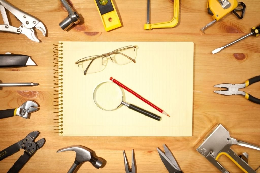 A wooden table displaying various tools alongside a notepad and pencil, suggesting a workspace for projects or repairs.